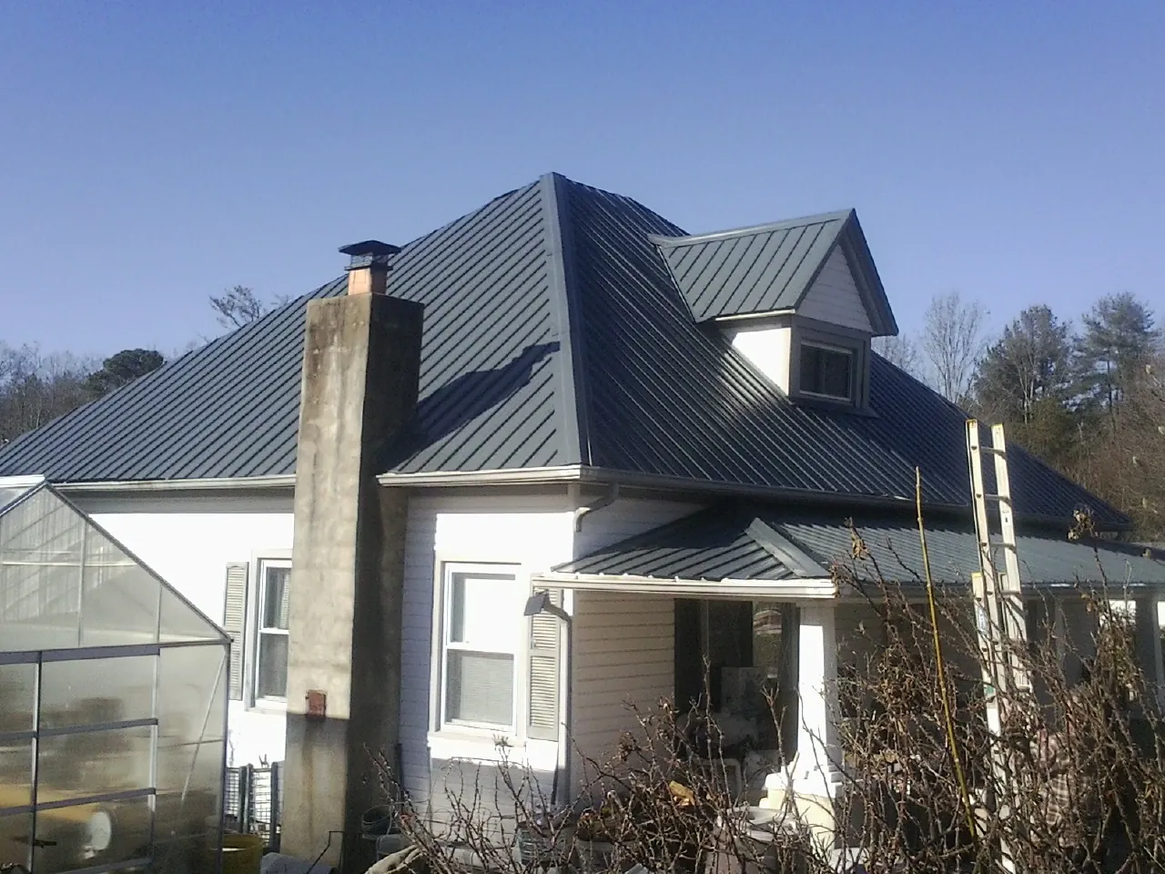 Dark blue standing seam metal roof on a white farmhouse with dormer — Slate & Tile Roof Repair by Roofing Brothers in Granite Springs