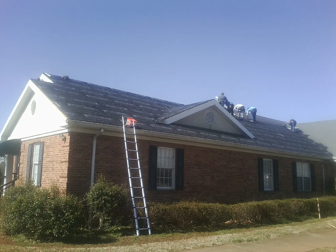 Crew tearing shingles off a brick ranch roof with a ladder set — Emergency Roof Repair work by our crew in Granite Springs