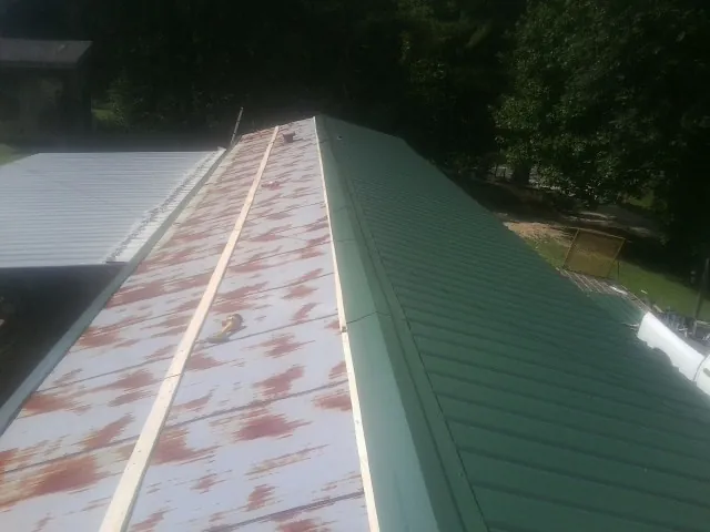 Old rusted panels beside newly installed green metal roofing — Wind Damage Roof Repair by Roofing Brothers in Granite Springs