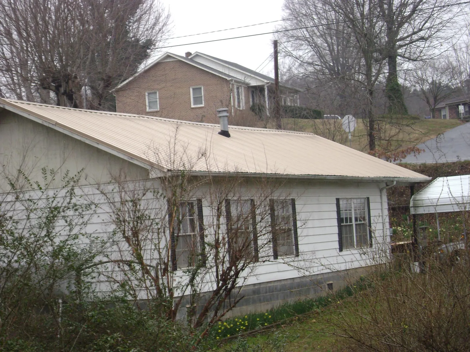 Tan metal roof on a white sided house set into a hillside — Commercial Roofing by Roofing Brothers in Granite Springs
