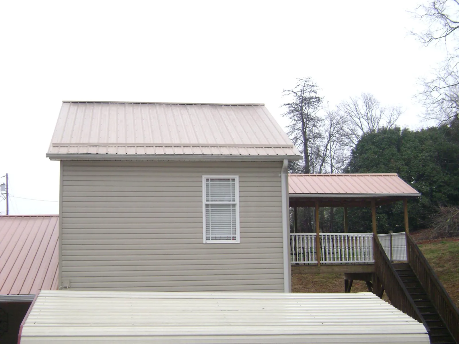 Tan metal roofs on a two story addition and attached porch, from a Roof Replacement job in Granite Springs